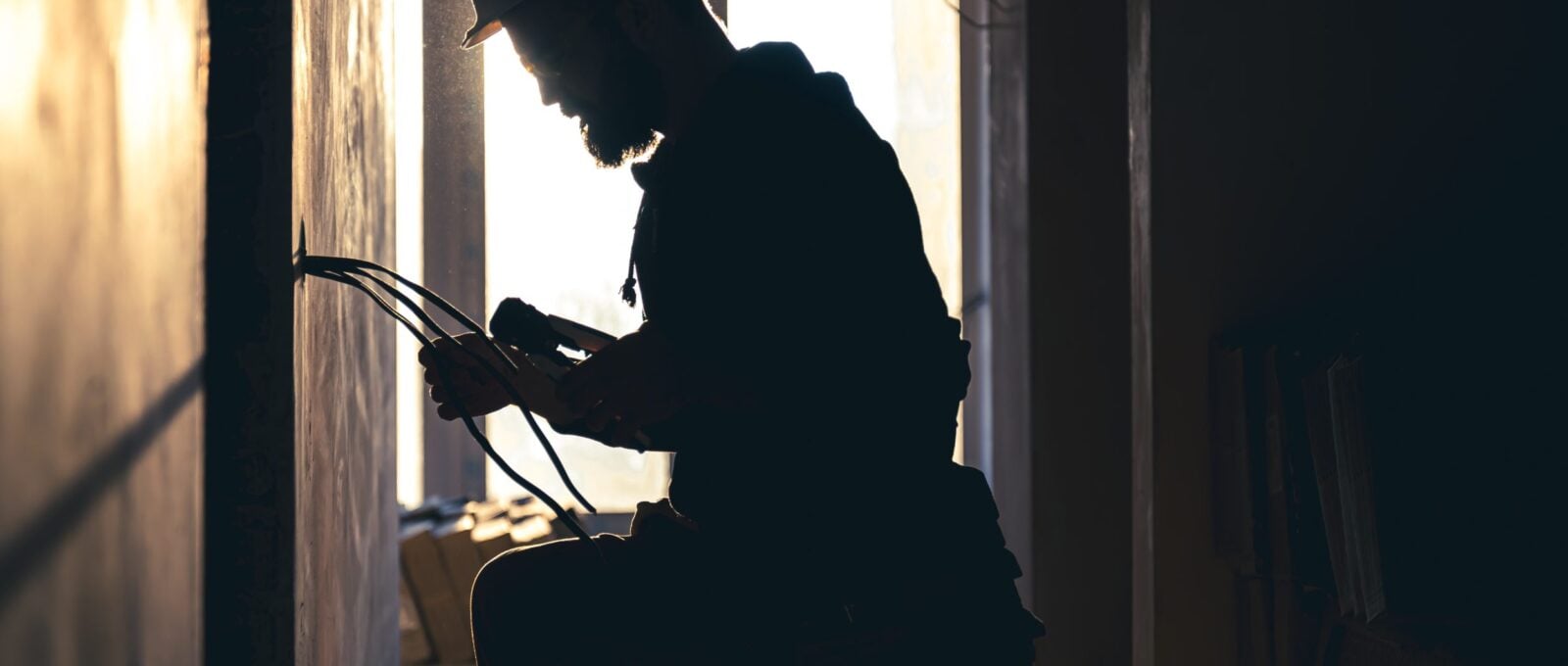 A construction electrician cuts a voltage cable during a repair, silhouette in the light of the setting sun.