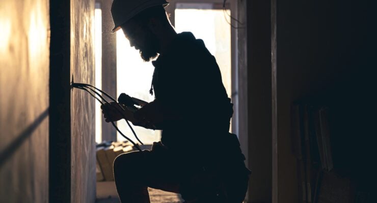 A construction electrician cuts a voltage cable during a repair, silhouette in the light of the setting sun.